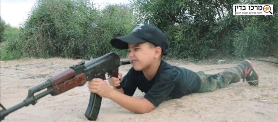 ילד עזתי שוכב בחול ואוחז ברובה קלצ'ניקוב