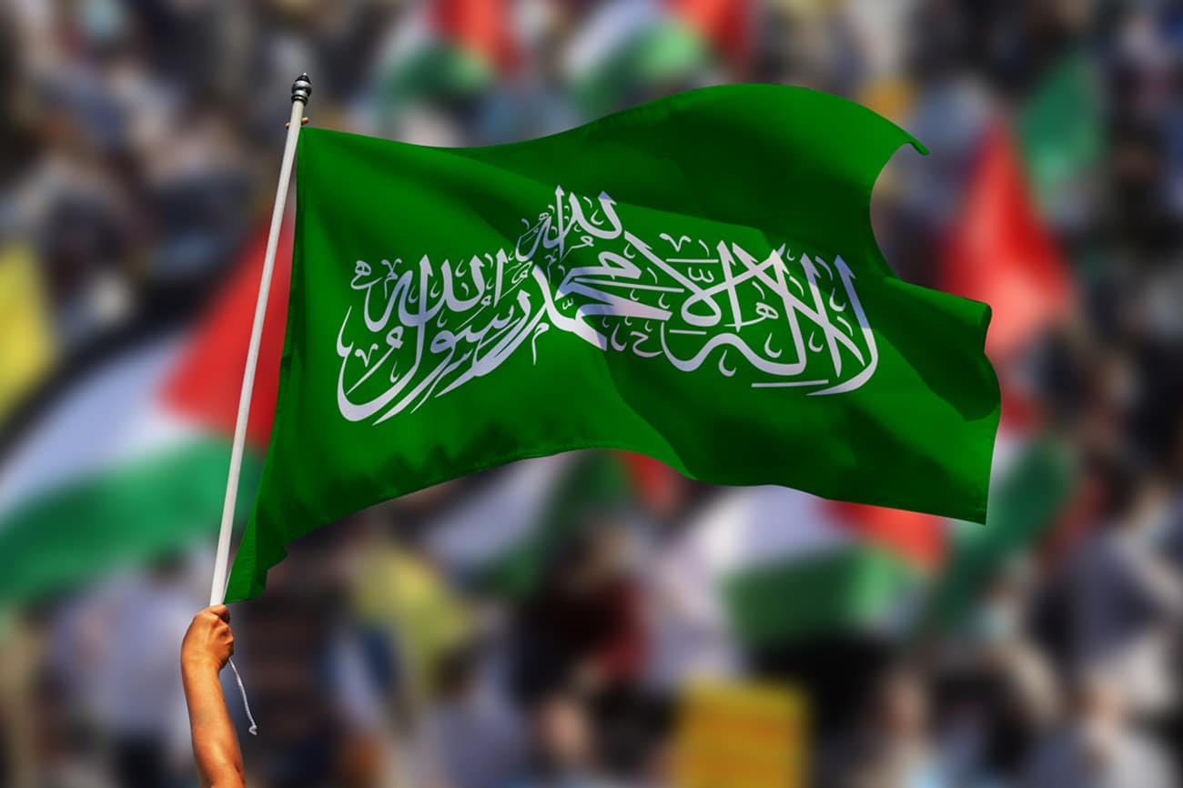 hand holding hamas green flag, in the background demonstrators with palestinian flags